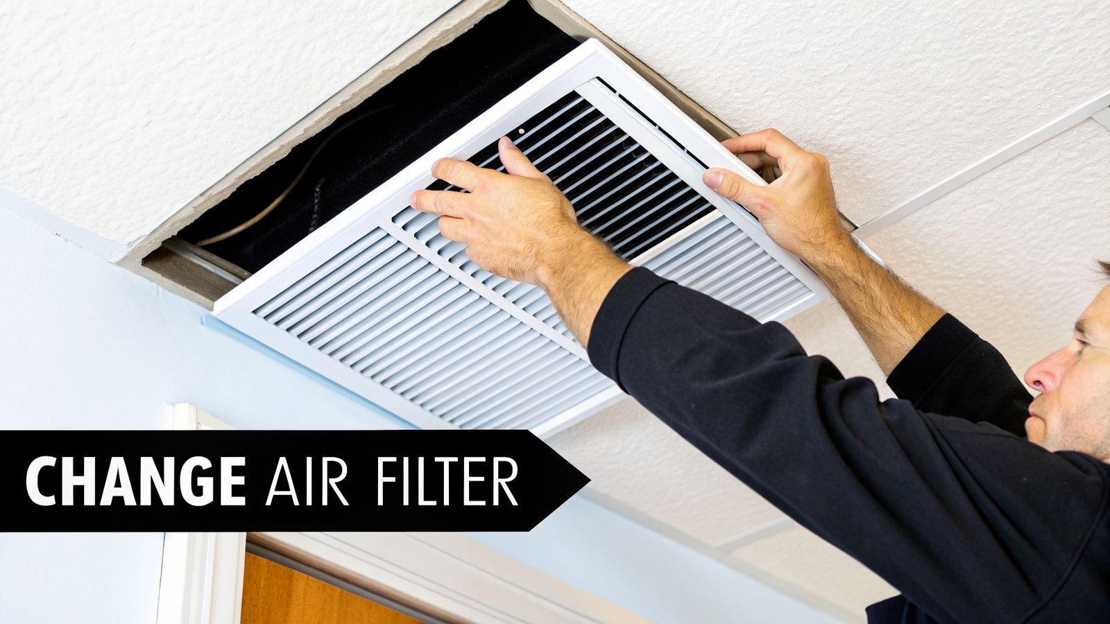 A person's hands are removing a white louvered air vent cover from a ceiling to access a filter.
