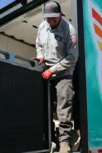 A worker in uniform and red gloves unloads a large, dark rectangular object from a truck on a sunny day—a glimpse into the hands-on careers and jobs available in our team.
